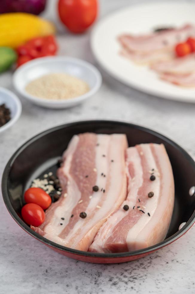 Pork belly in a pan with pepper seeds, tomatoes and spices photo