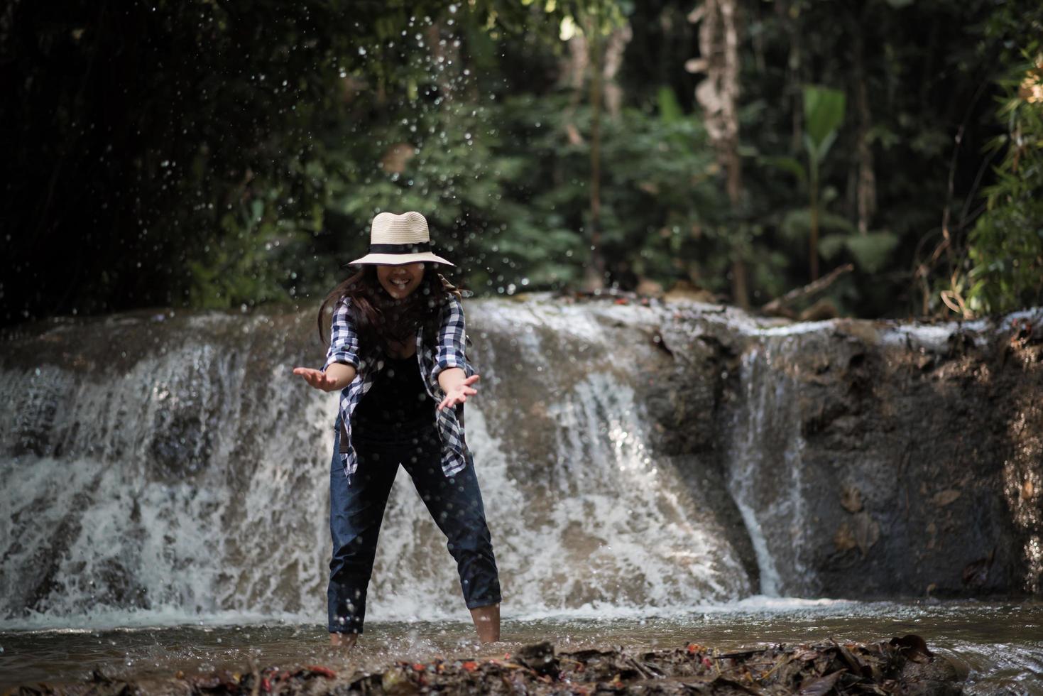 Young woman having fun under a waterfall in the forest photo