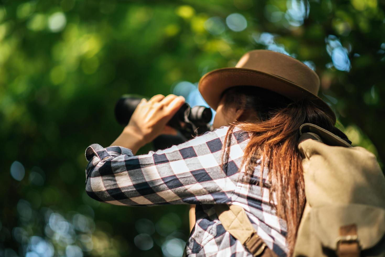 Feliz joven aventurera viendo la vida silvestre con binoculares en la naturaleza foto