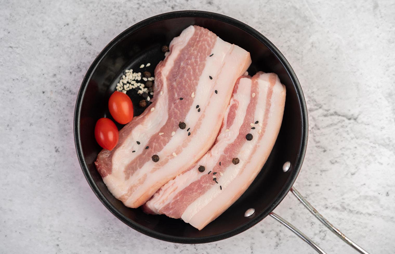 panceta de cerdo en una sartén con semillas de pimiento, tomates y especias foto