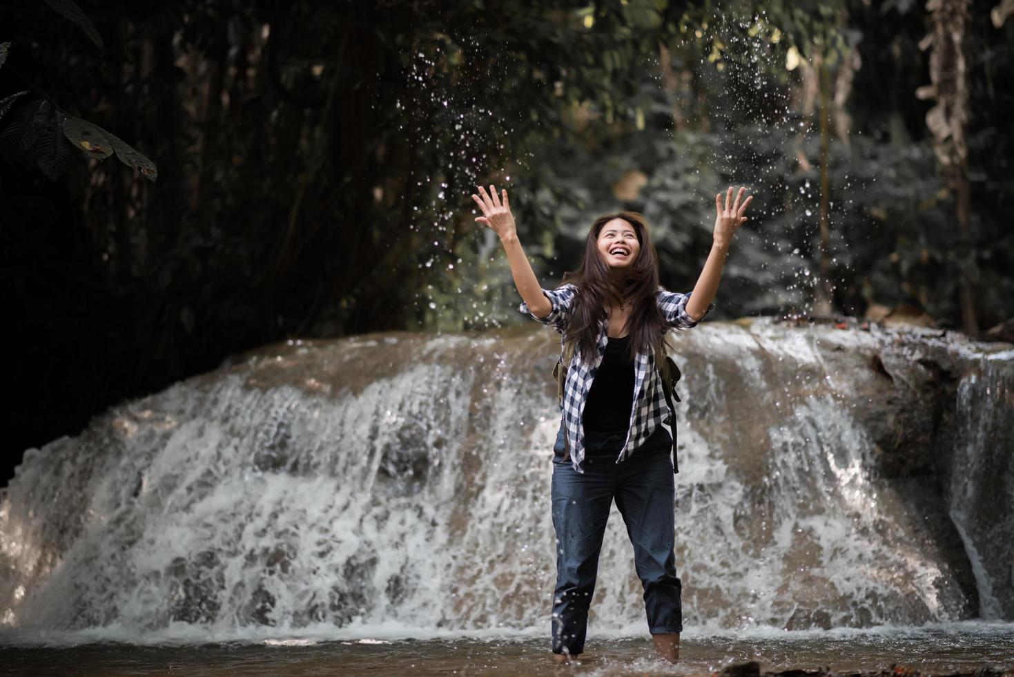 Young woman having fun under a waterfall in the forest photo