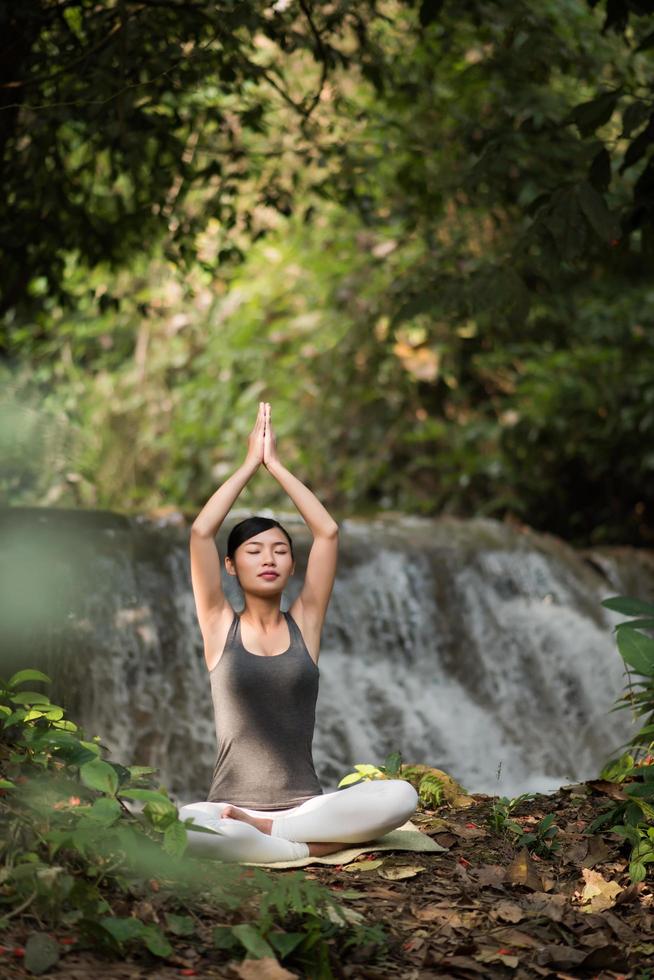 mujer joven en una pose de yoga sentado cerca de una cascada foto