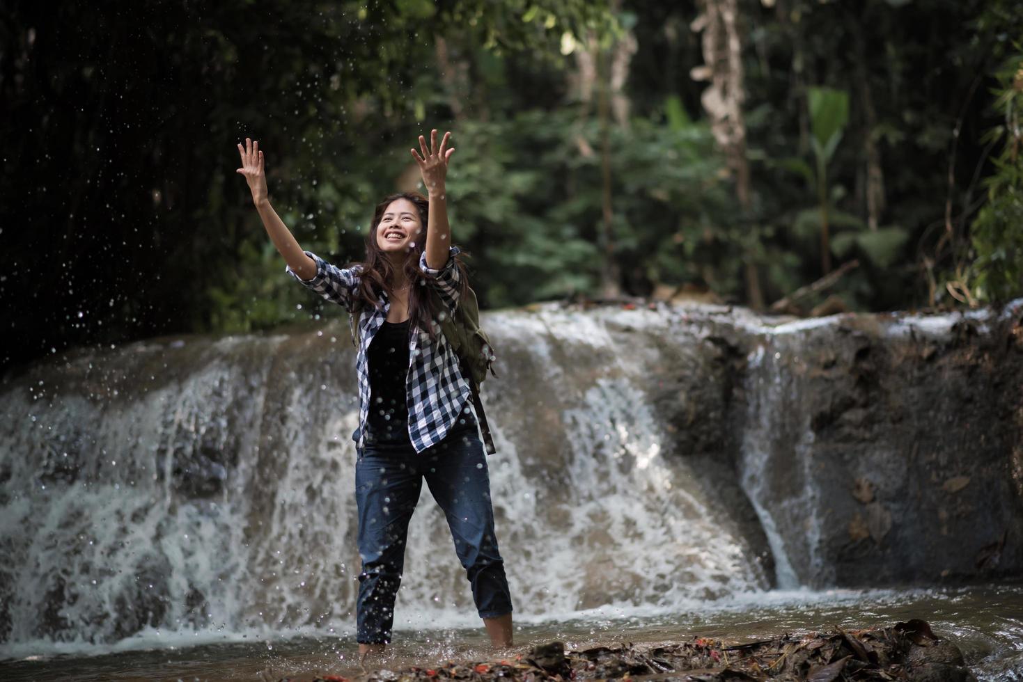 Mujer joven divirtiéndose bajo una cascada en el bosque foto