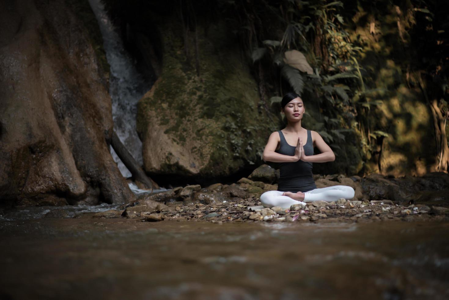 mujer joven en una pose de yoga sentado cerca de una cascada foto