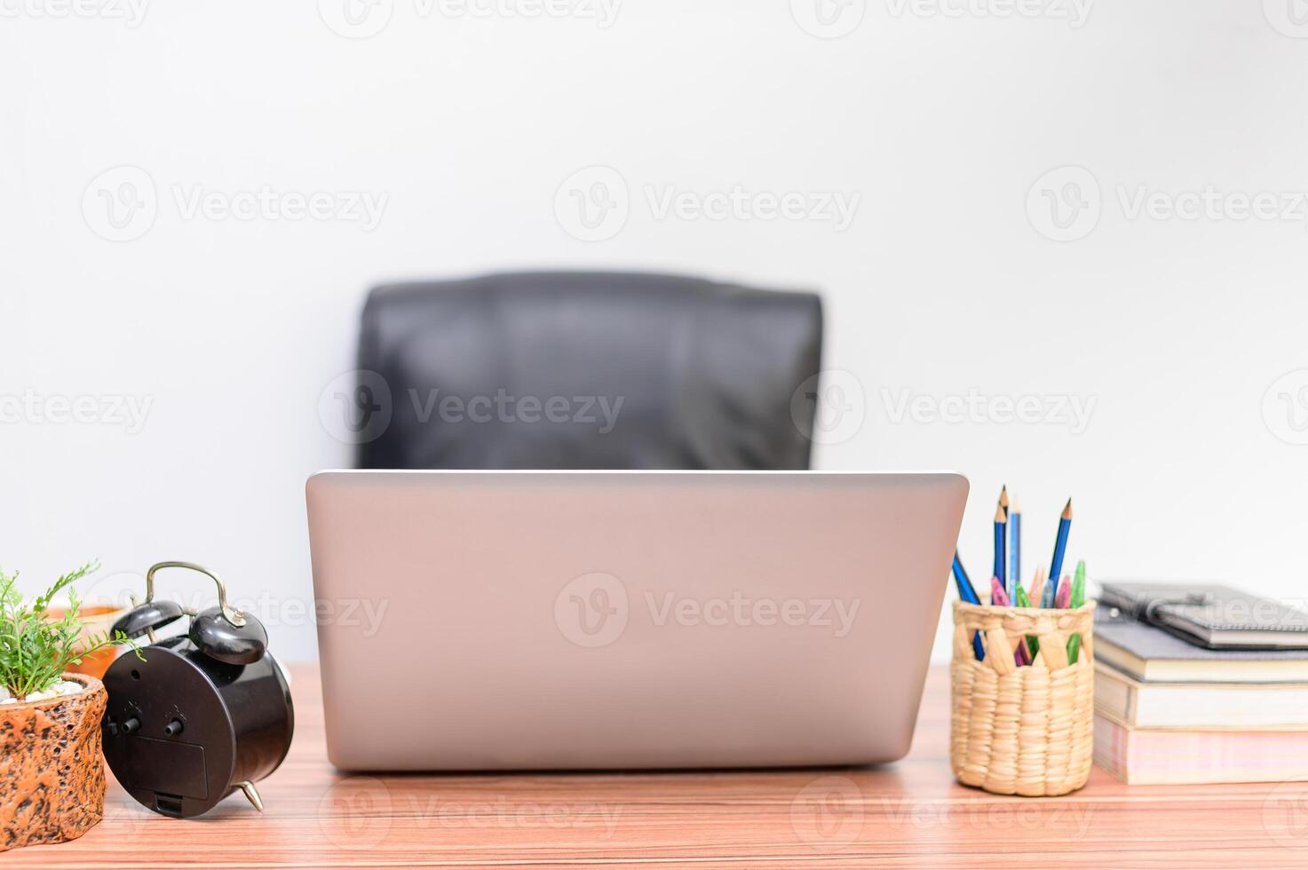 A laptop sitting on a desk with a clock, books and a plant photo