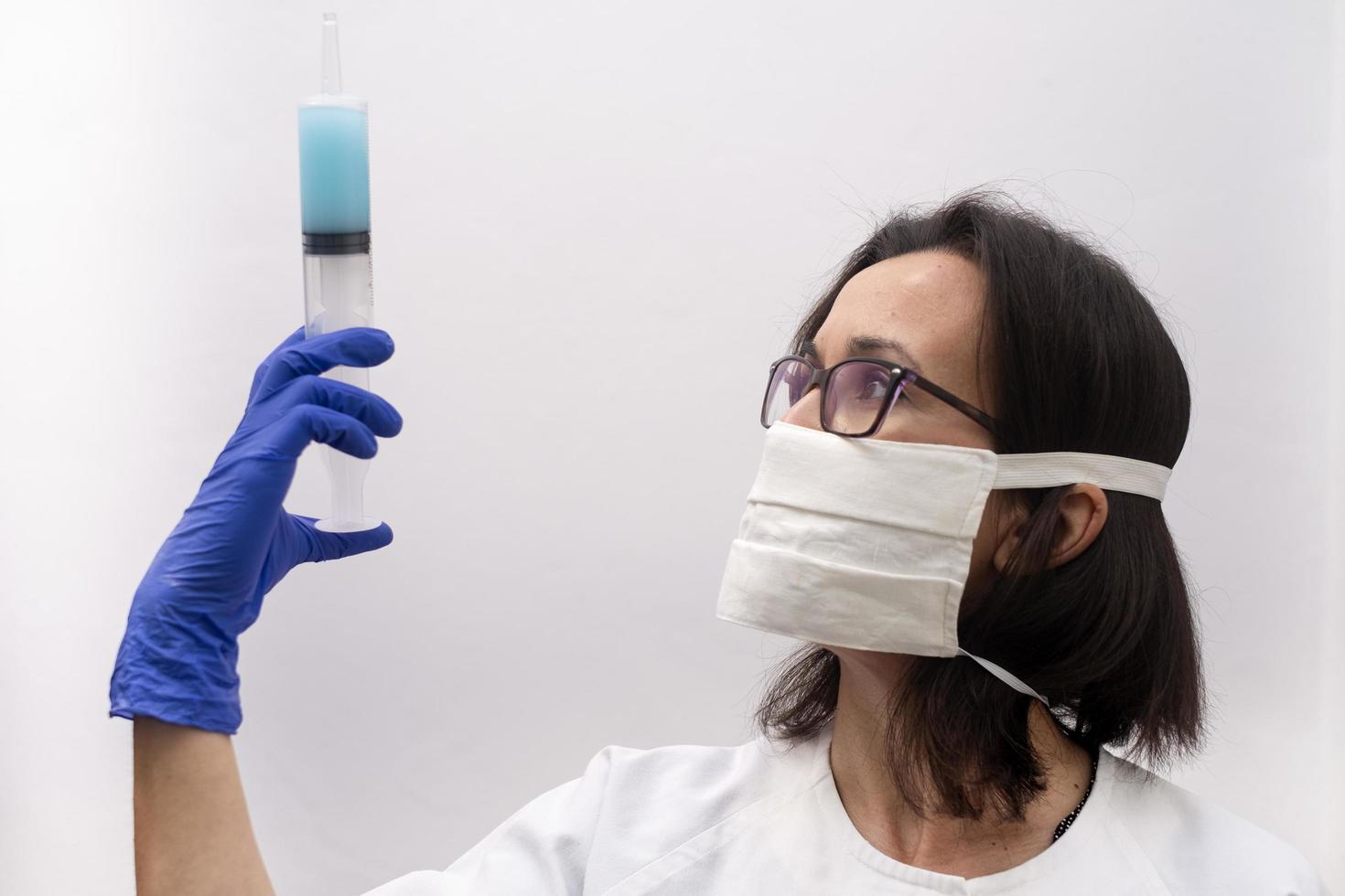 A nurse wearing a mask and gloves holding a syringe of virus vaccine in a modern clinic photo