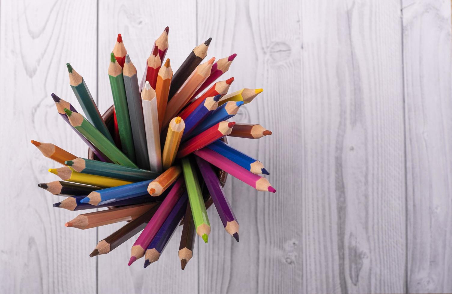 Colored wooden pencils, in a brown leather beaker, seen from above, with white and gray wooden background photo