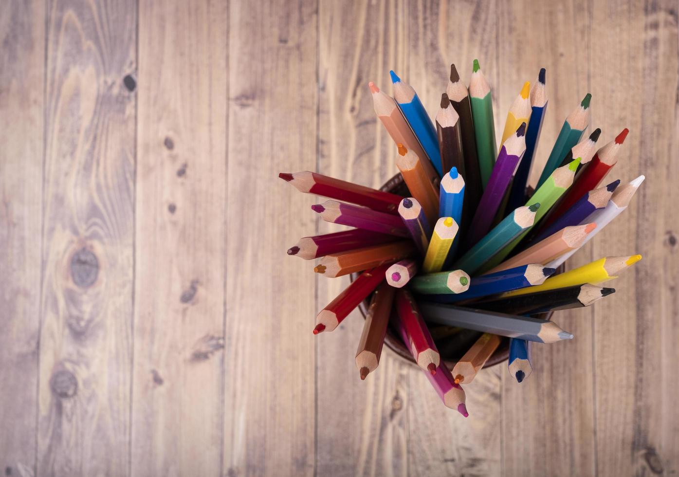 Colored wooden pencils, in a brown leather beaker, seen from above, with wooden background photo