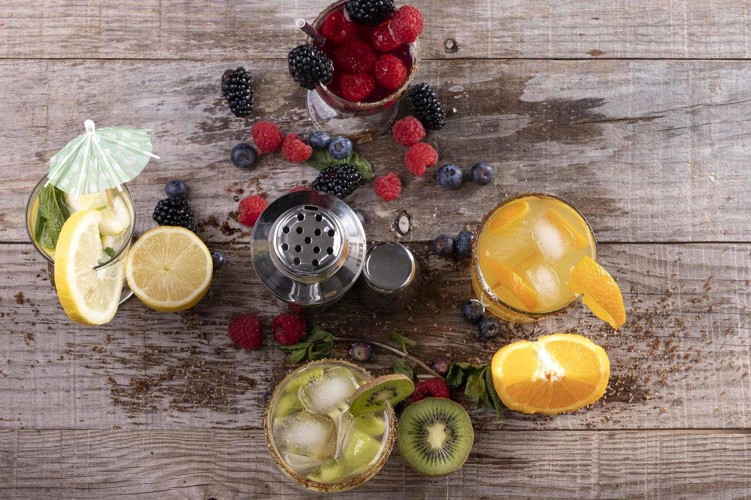 diferentes tipos de jugos de frutas acompañados de una coctelera de metal sobre una base de madera. concepto de vida saludable foto