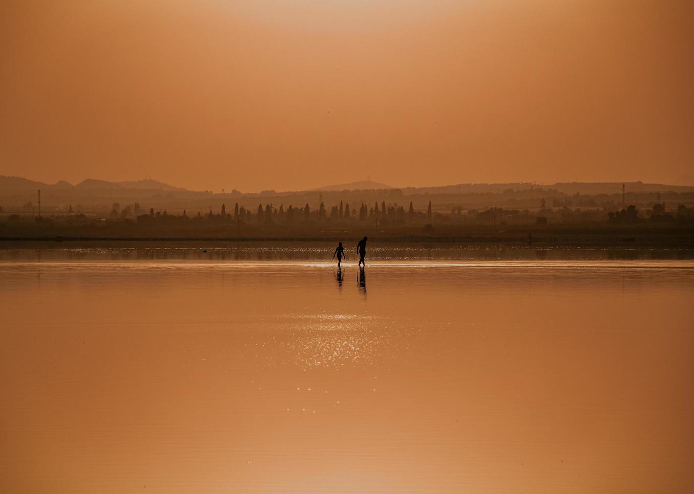 Silhouette of 2 people standing on body of water during sunset photo