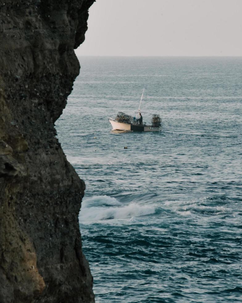 White boat on sea beside brown rock formation during daytime photo