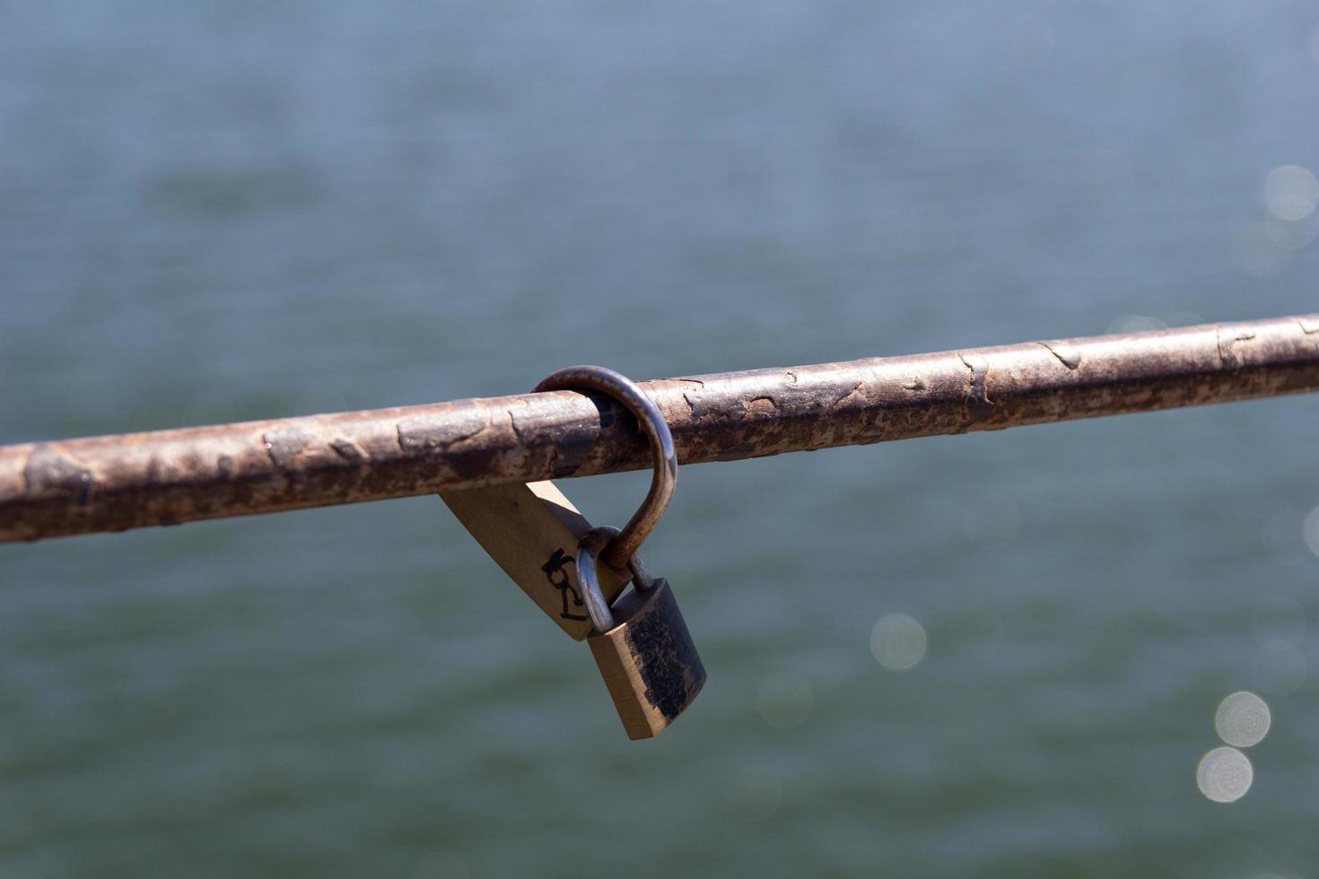 A padlock on a metal bar with water in the background photo