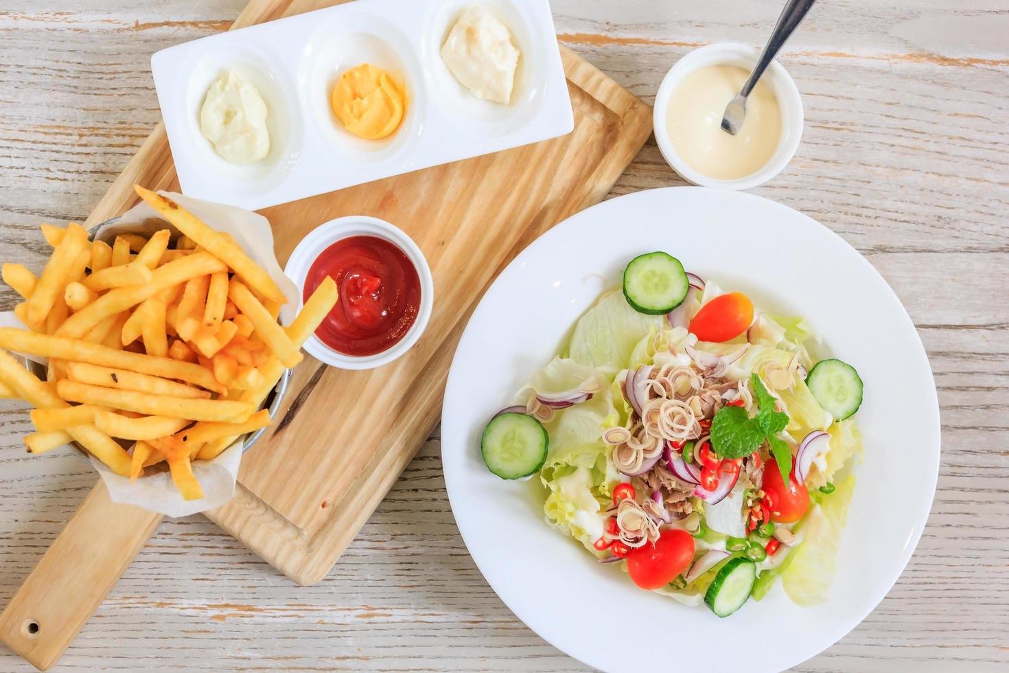 papas fritas y salsa de tomate en un plato de madera y ensalada con verduras frescas y atún, vista superior con espacio libre para el texto. foto