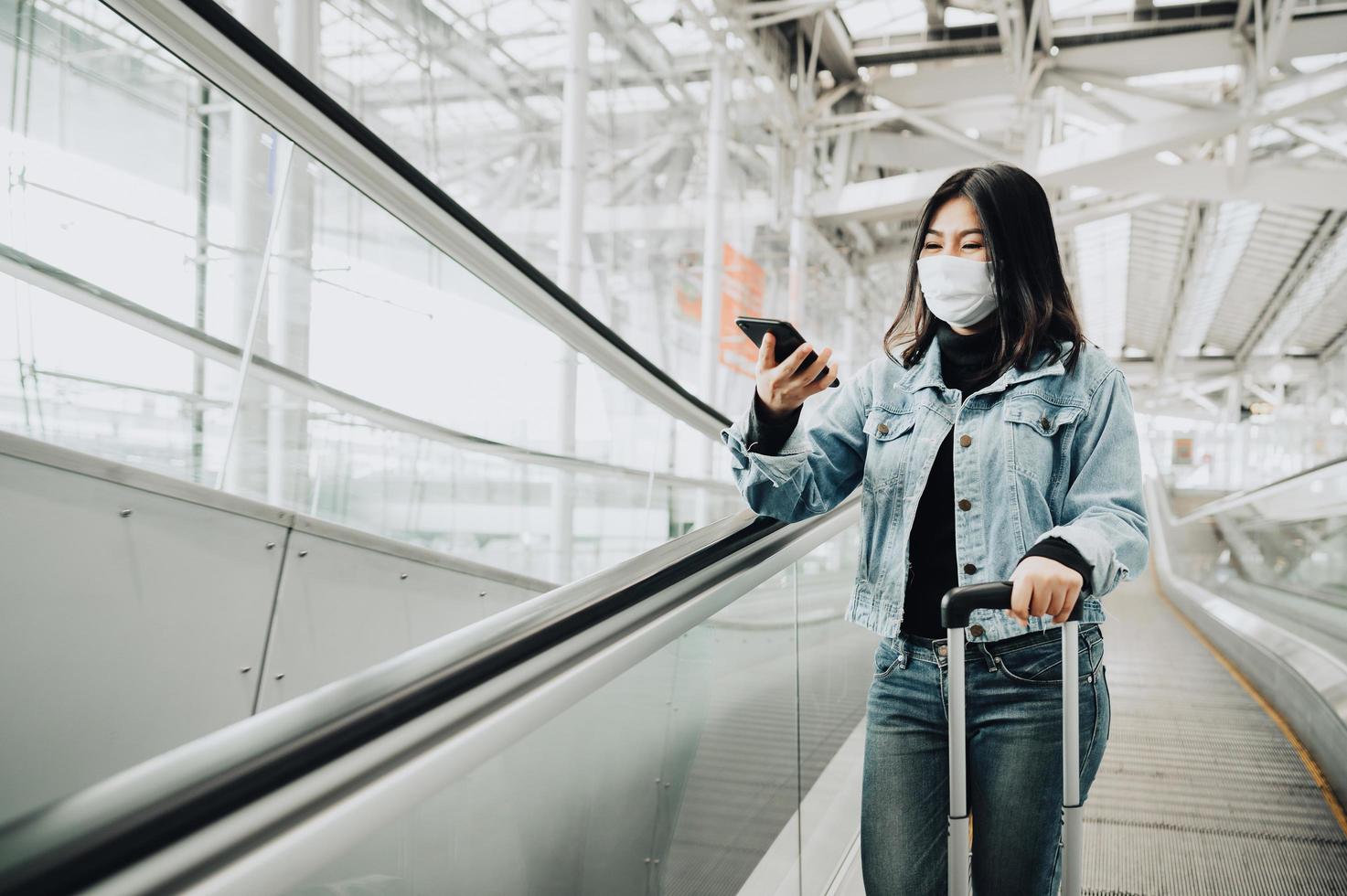 Woman on an escalator wearing a mask and holding a phone photo