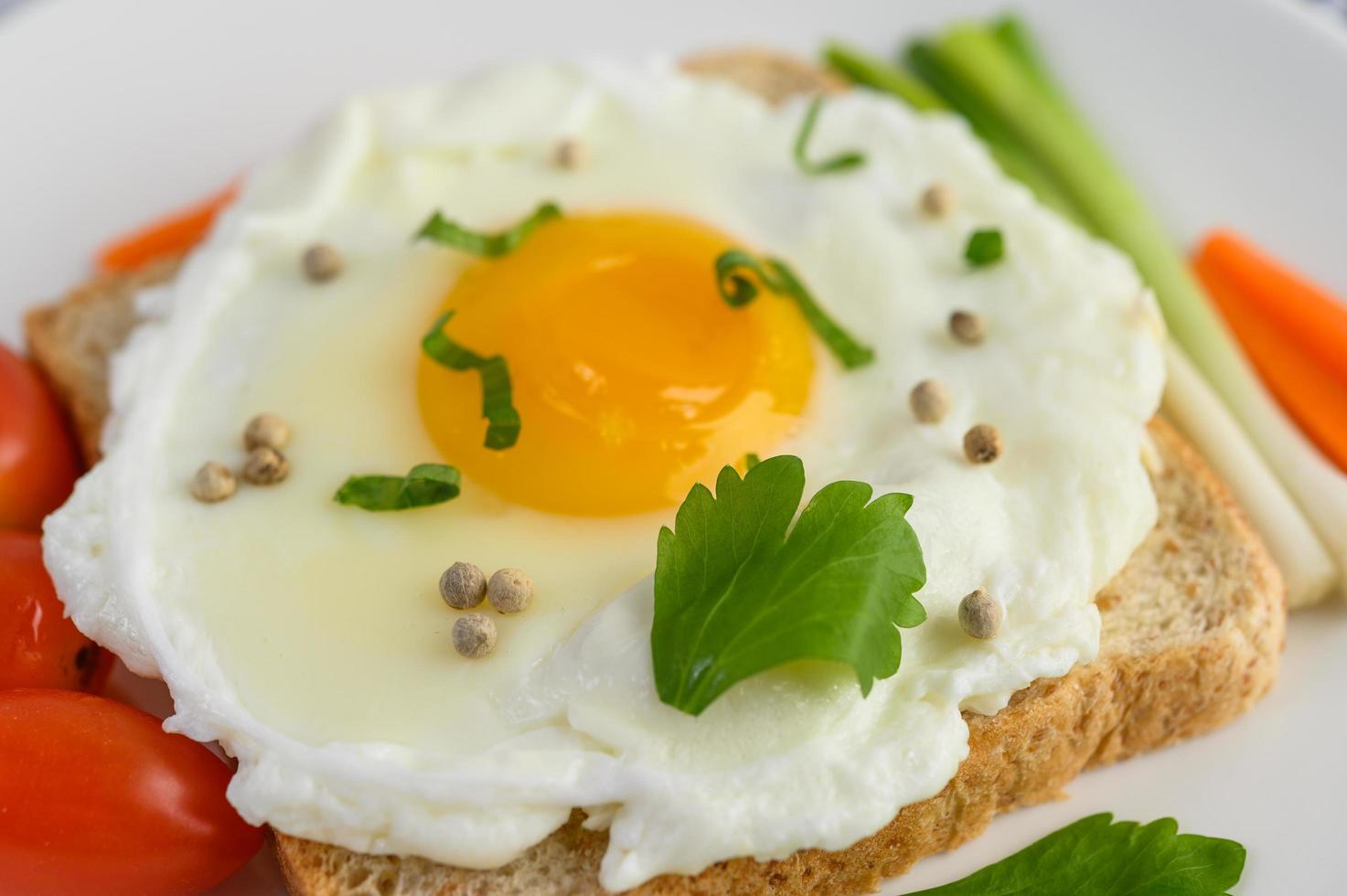 A fried egg on toast topped with pepper seeds with carrots and spring onions photo