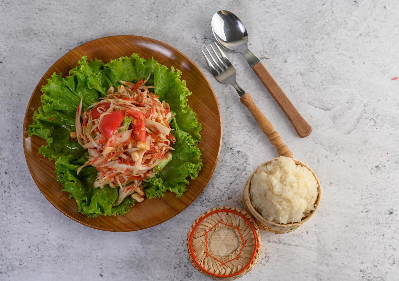 ensalada tailandesa de papaya con arroz glutinoso, cuchara y tenedor foto