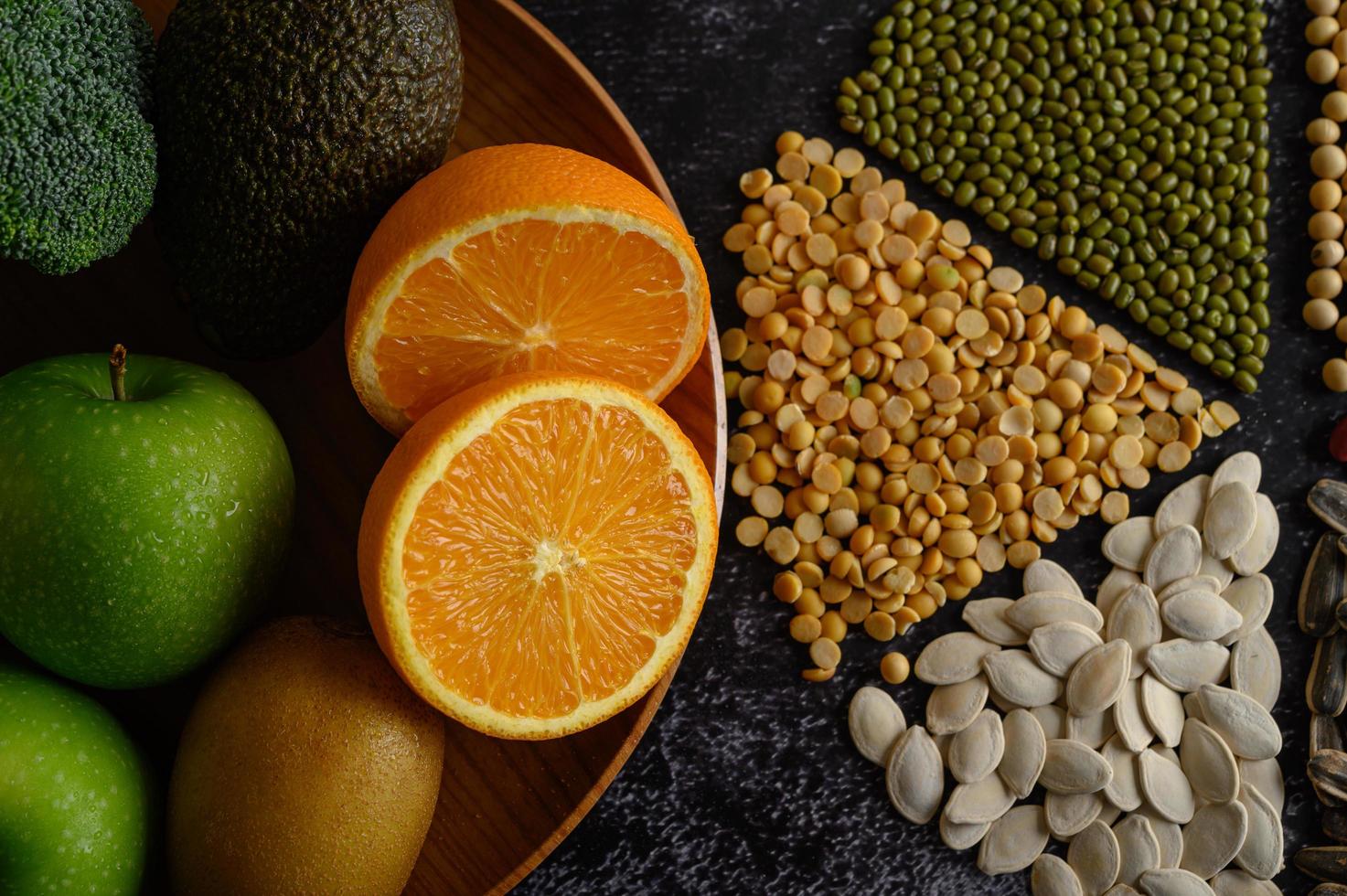 legumbres con naranjas, kiwi y manzana sobre un fondo negro foto