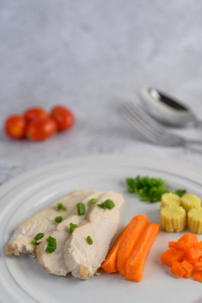 Steamed chicken breast on a white plate with spring onions, baby corn and carrots photo