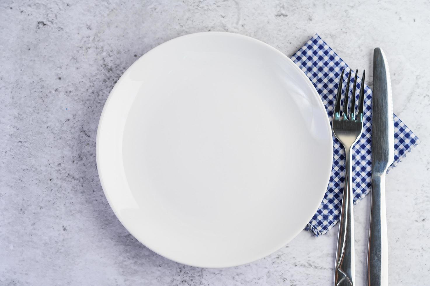 Empty white plate with fork and a knife on a blue-white tablecloth photo