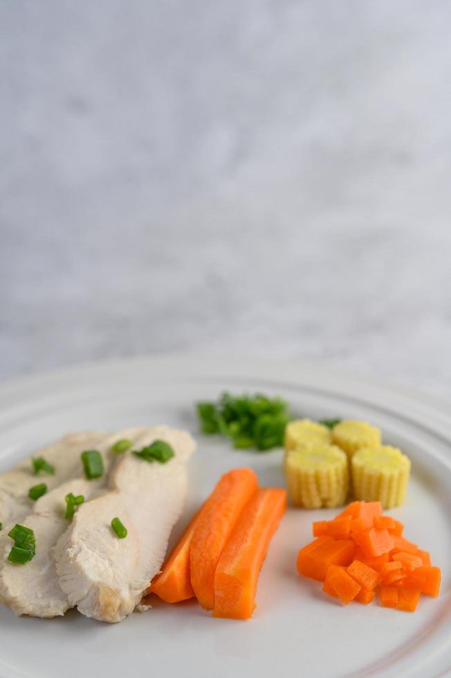 Steamed chicken breast on a white plate with spring onions, baby corn and carrots photo