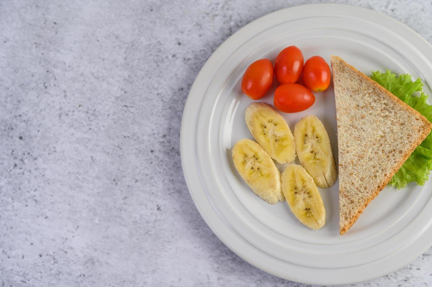 Pan con plátano y tomates en una placa blanca. foto