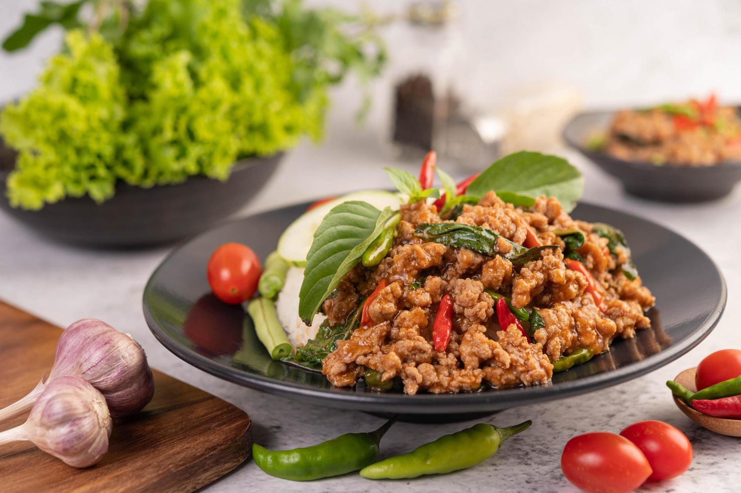 Ensalada picante de cerdo picada con arroz, chili y tomates en una placa negra foto