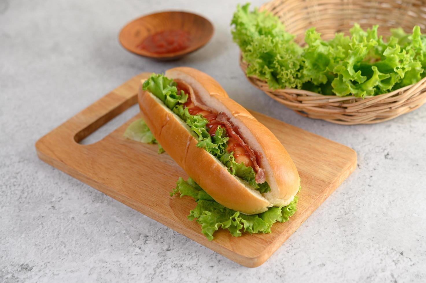 Hotdog con lechuga y tomate sobre una tabla para cortar madera foto