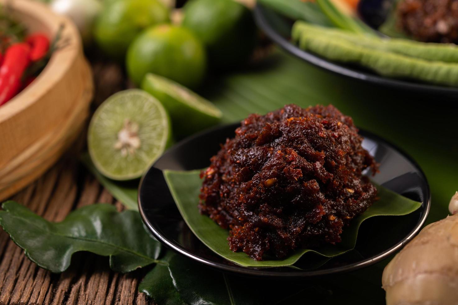 Chili paste served on banana leaves surrounded by long beans, lime, chili and eggplant photo