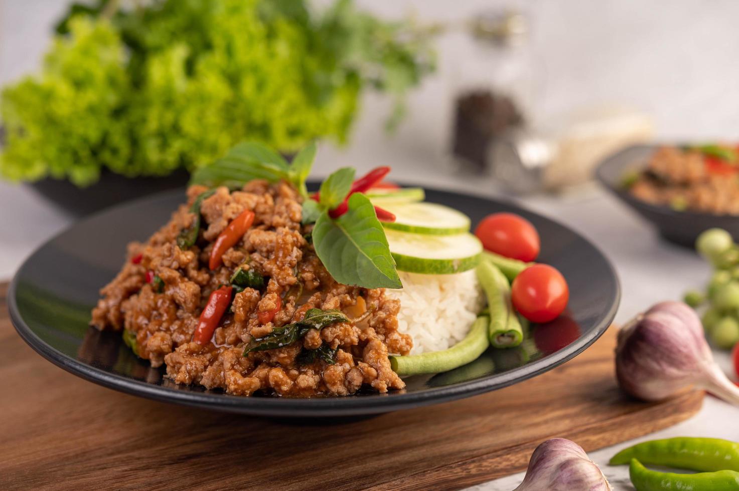 Ensalada picante de cerdo picada con arroz, chili y tomates en una placa negra foto