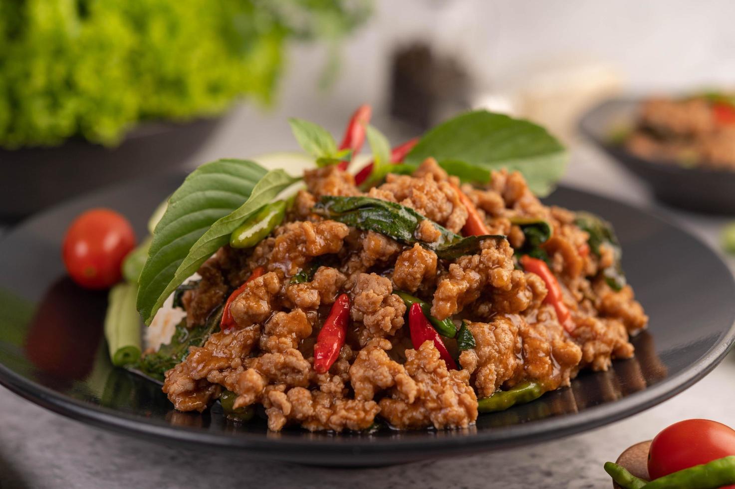 Spicy minced pork salad with rice, chili's, and tomatoes on a black plate photo