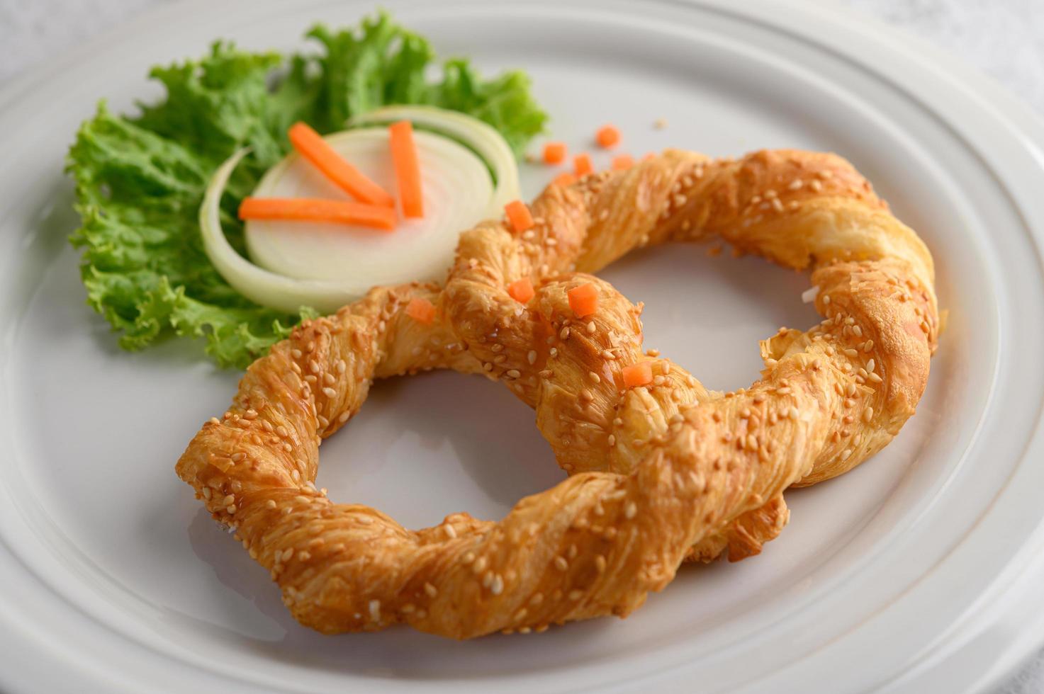 Pretzel on a white dish with lettuce and carrots photo