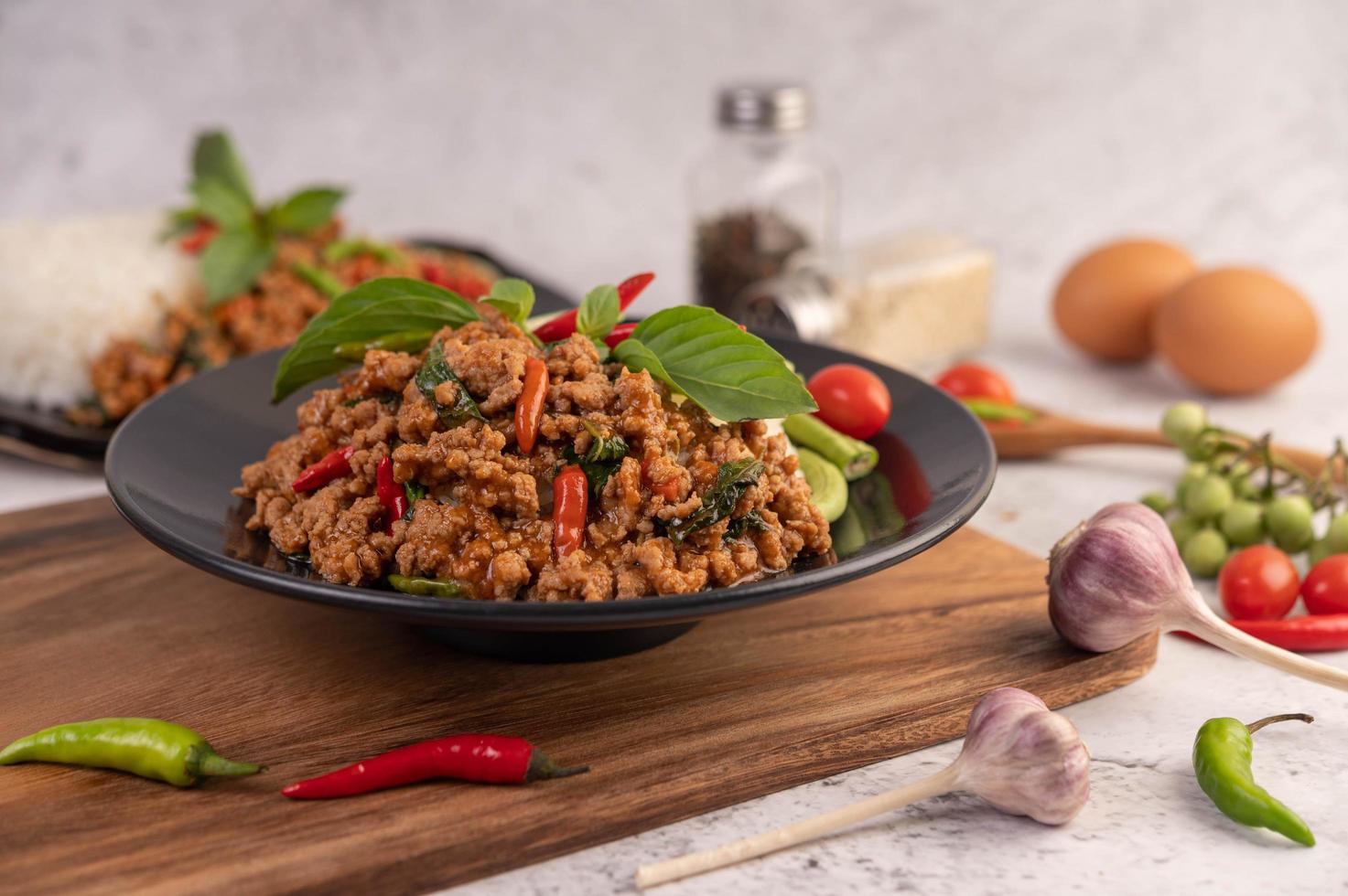 Ensalada picante de cerdo picada con arroz, chili y tomates en una placa negra foto