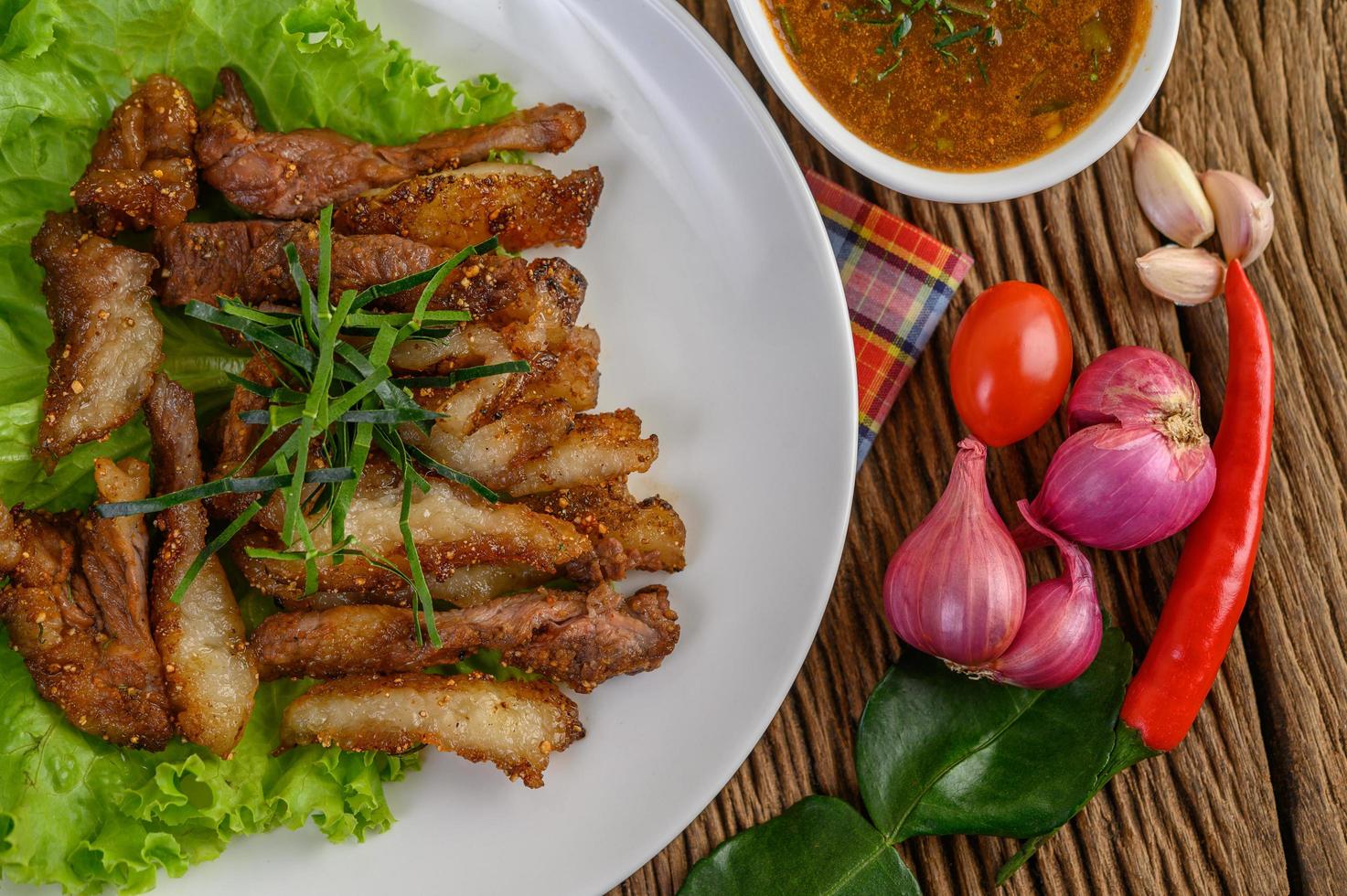 Pork neck grilled on a white plate with red onion, tomato and chili on a wooden table photo