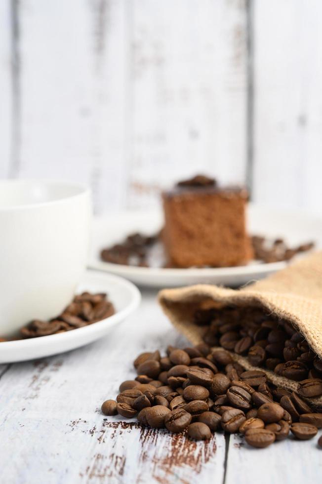 Granos de café en sacos de cáñamo sobre una mesa de madera blanca foto