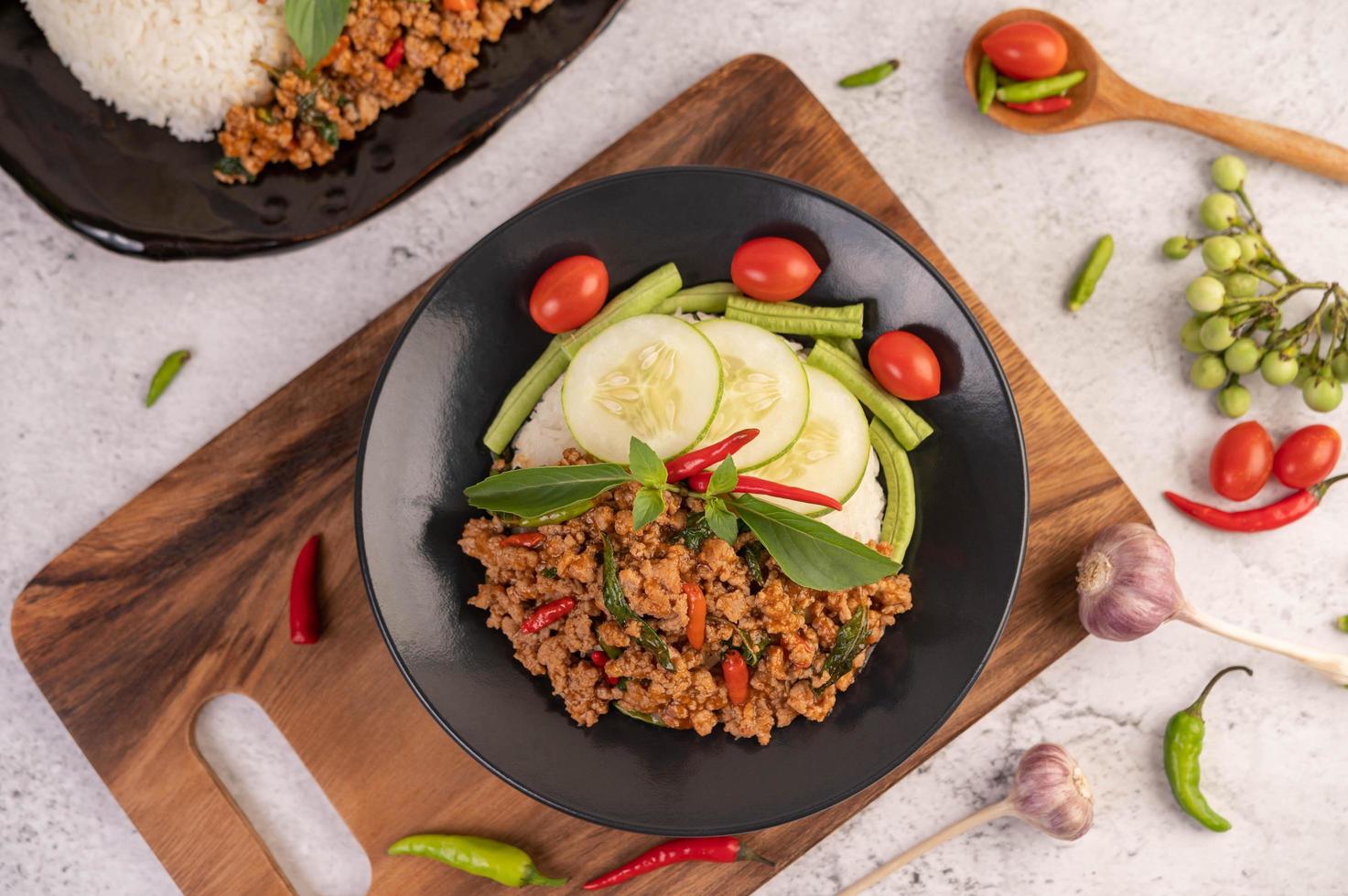 Ensalada picante de cerdo picada con arroz, chili y tomates en una placa negra foto