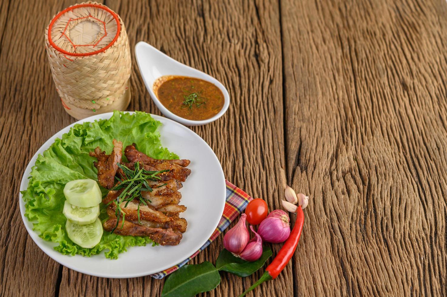 Pork neck grilled on a white plate with red onion, tomato and chili on a wooden table photo