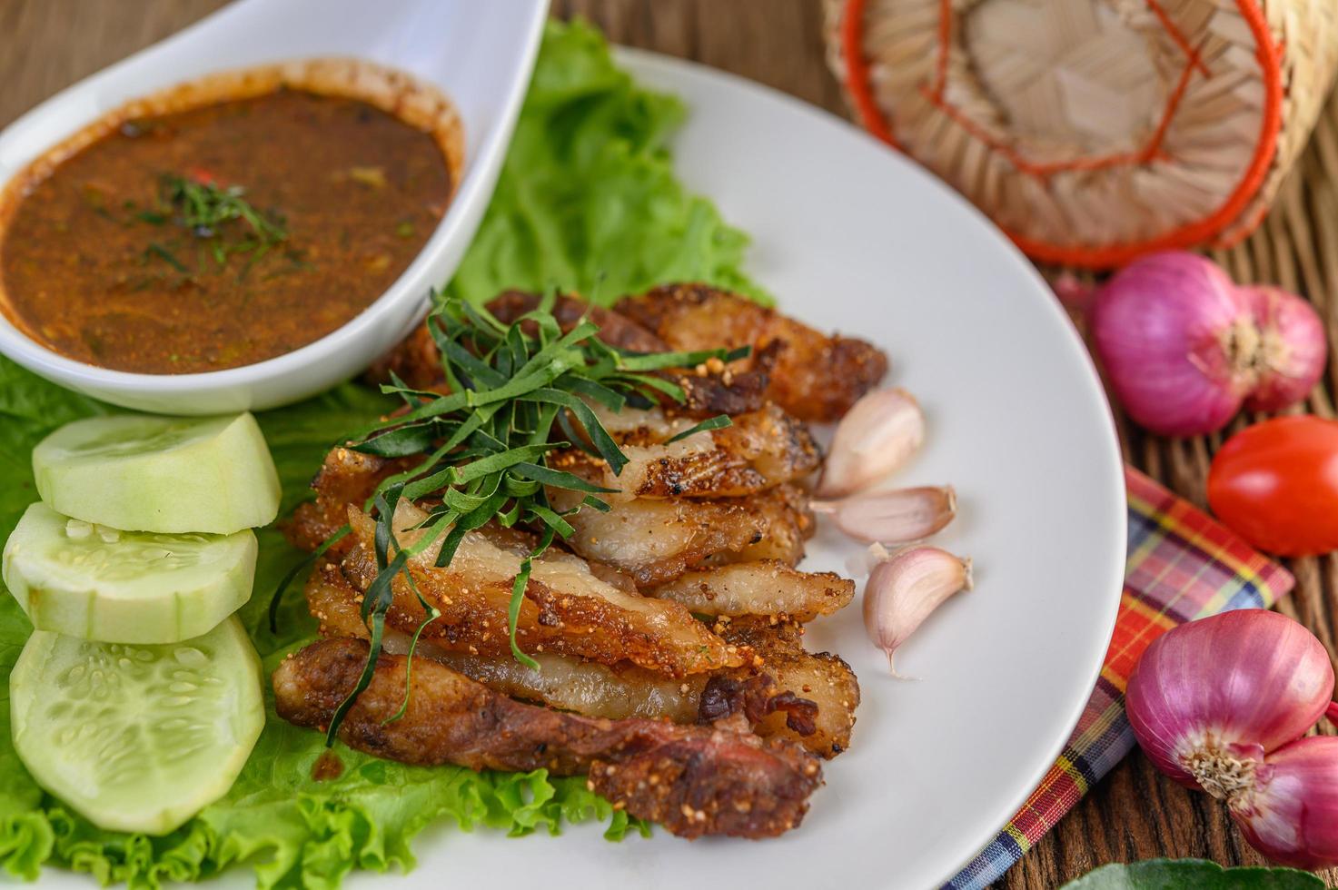 Pork neck grilled on a white plate with red onion, tomato and chili on a wooden table photo