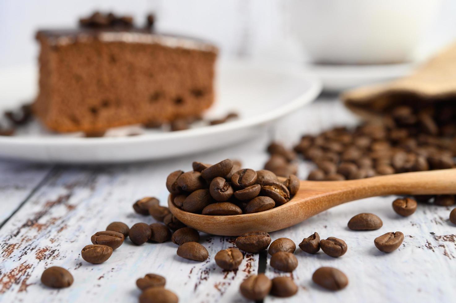 Granos de café en una cuchara de madera sobre una mesa de madera blanca foto