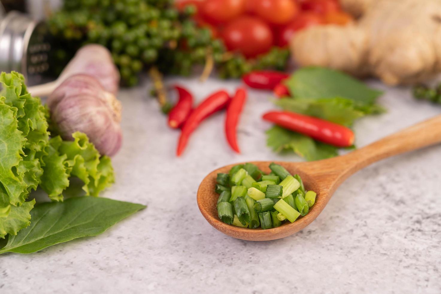 Chopped spring onion in a wooden spoon with peppers and tomatoes photo