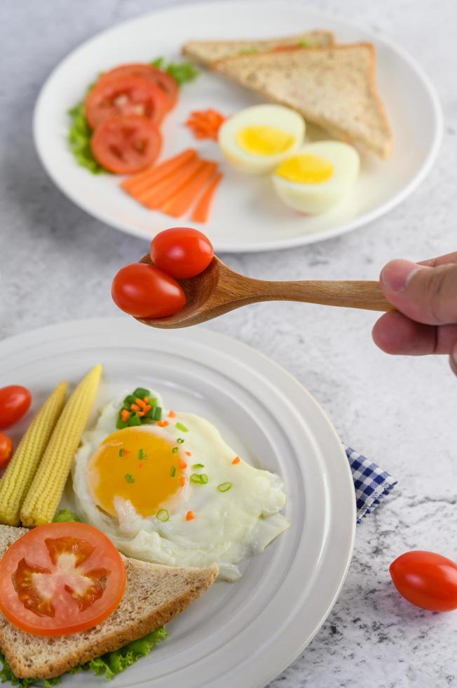 Huevos fritos, pan, zanahorias y tomates en una placa blanca. foto