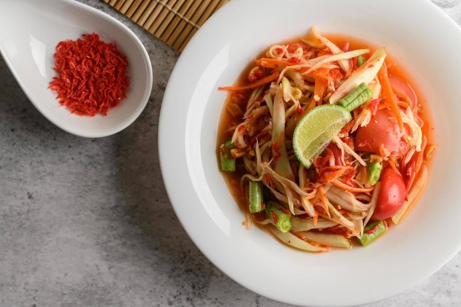 Ensalada de papaya tailandesa en un plato blanco con camarones secos foto