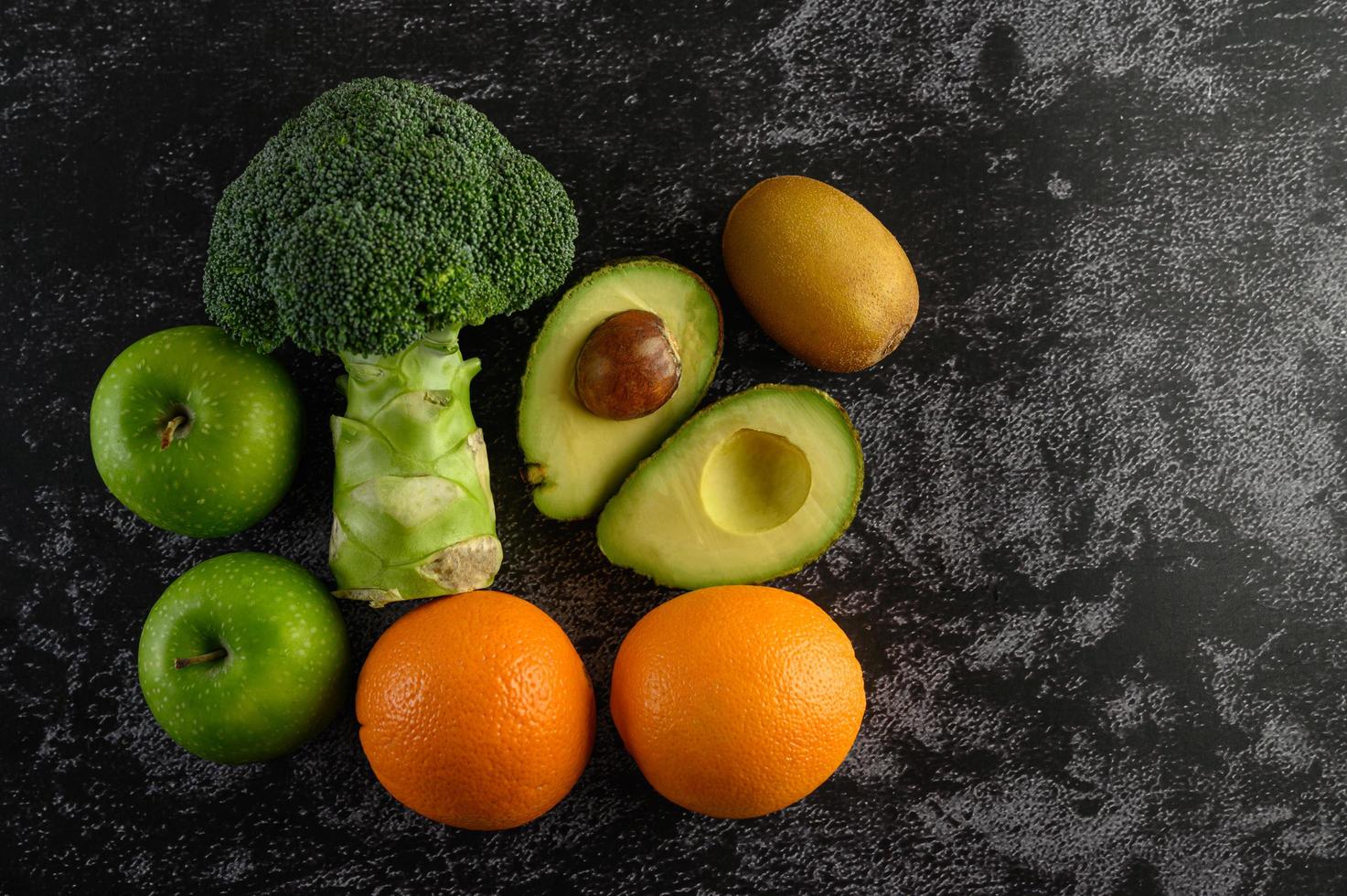 Broccoli, apple, orange, kiwi and avocado on a black cement floor background photo