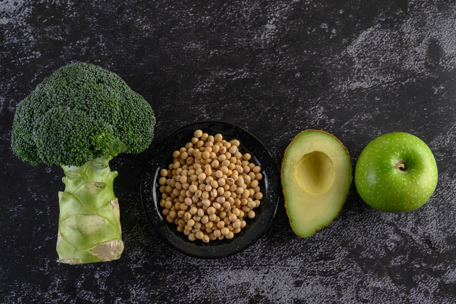 Broccoli, apple, avocado and beans on a black cement floor background photo