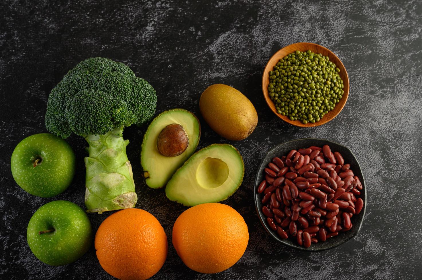 Broccoli, apple, orange, kiwi, avocado and beans on a black cement floor background photo