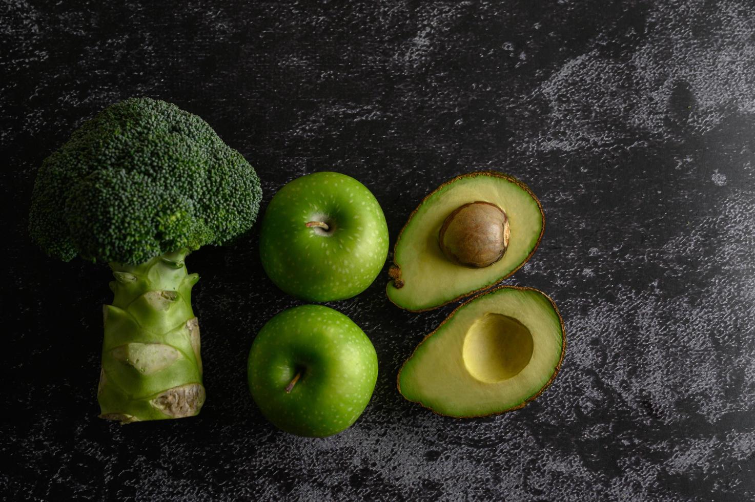 Broccoli, apple and avocado on a black cement floor background photo