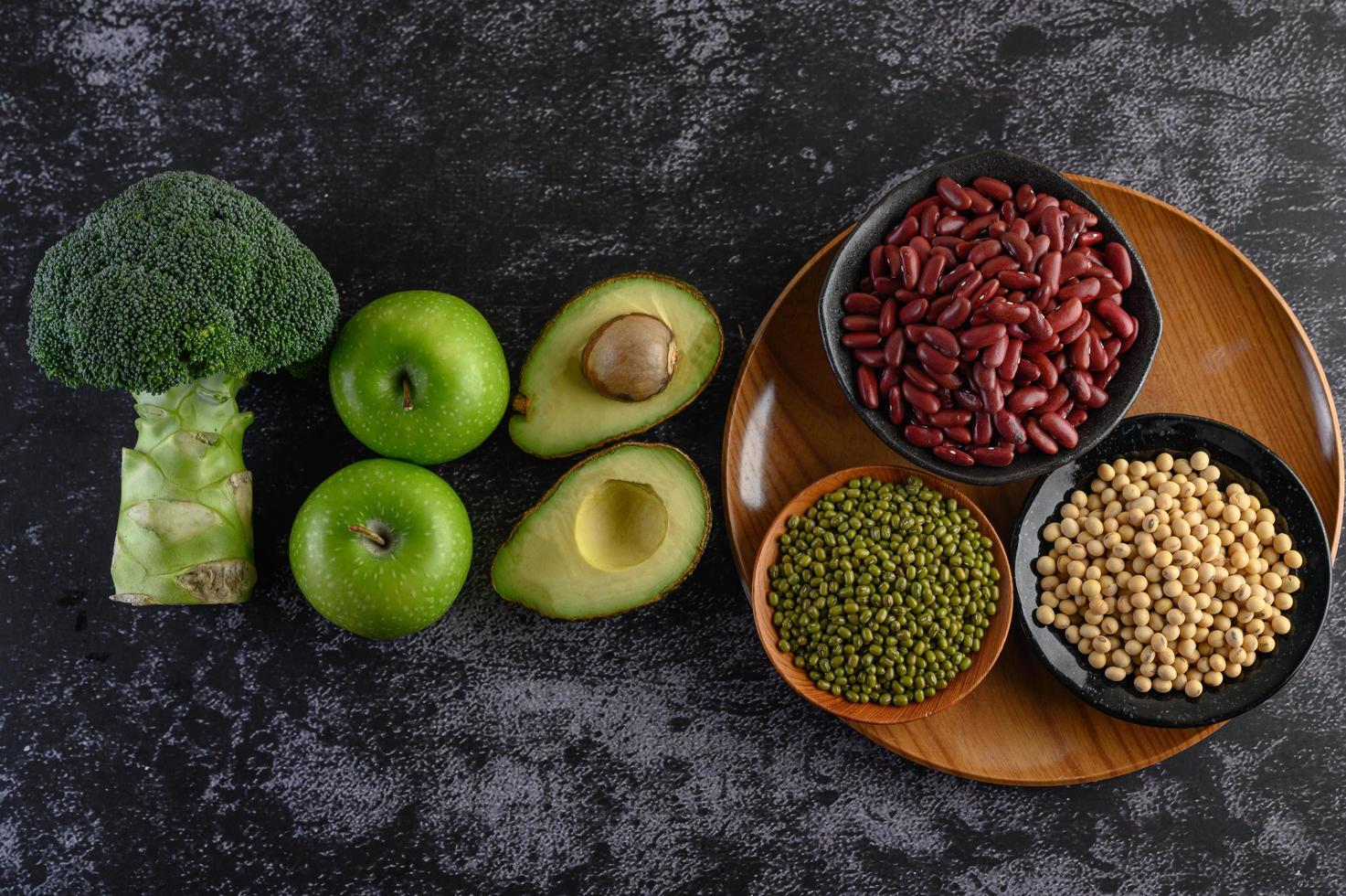 Brócoli, manzana y aguacate con frijoles sobre un fondo de piso de cemento negro foto