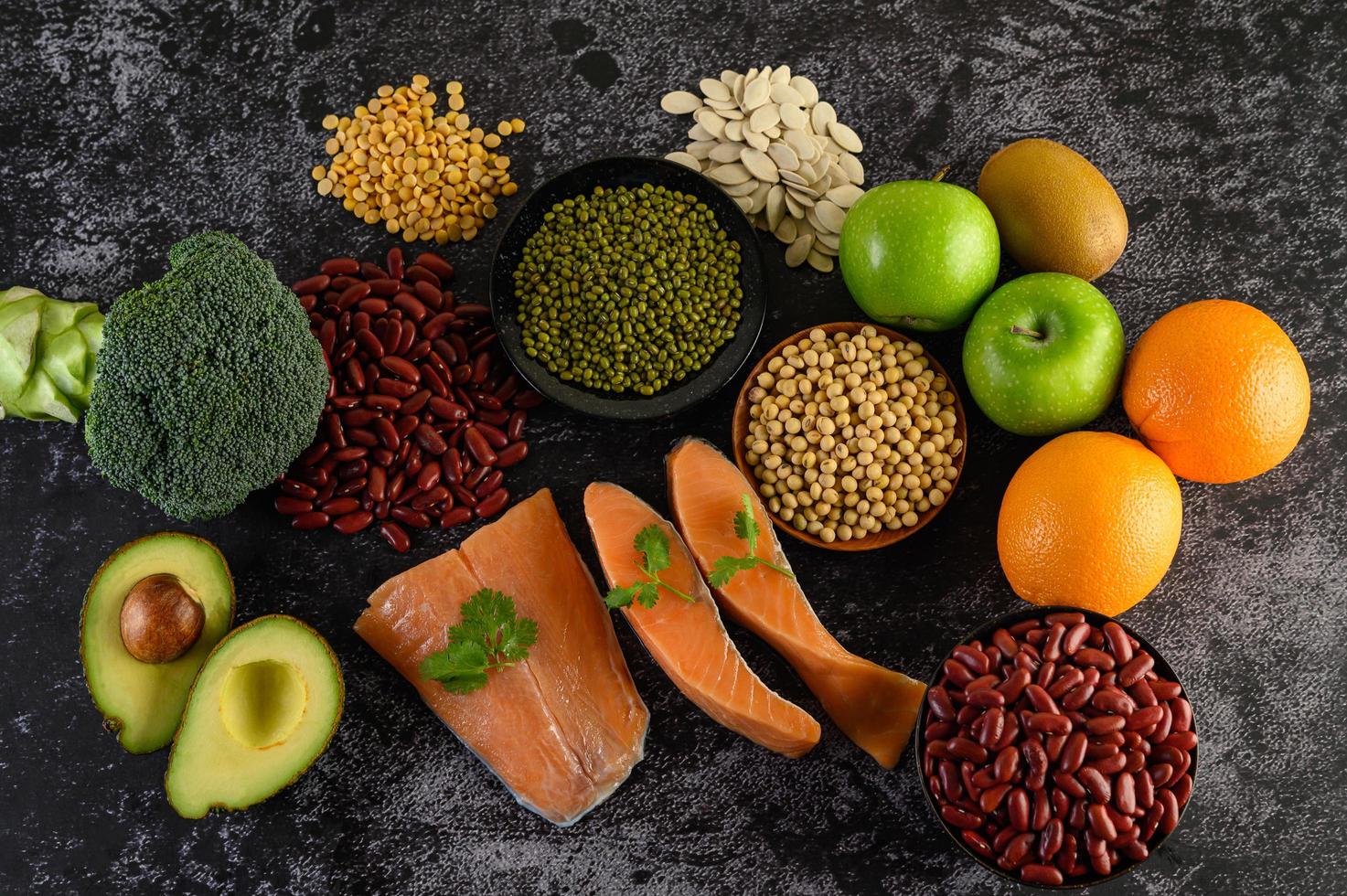 Legumes, broccoli, fruit, and salmon on a black cement background photo