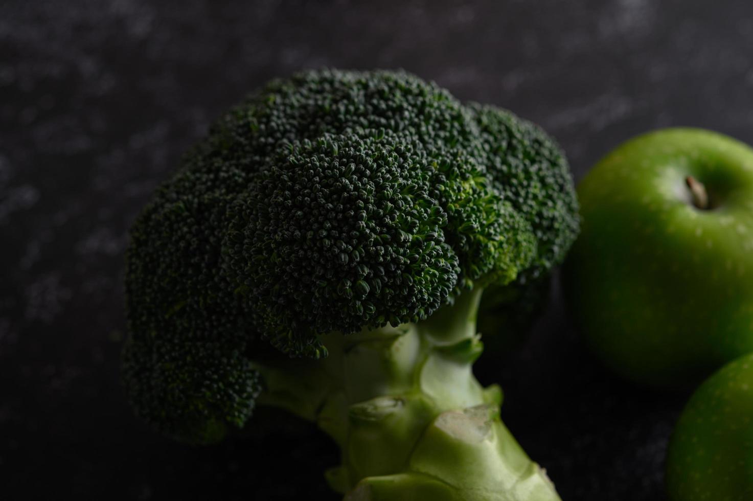 Brócoli, manzana y aguacate sobre un fondo de piso de cemento negro foto