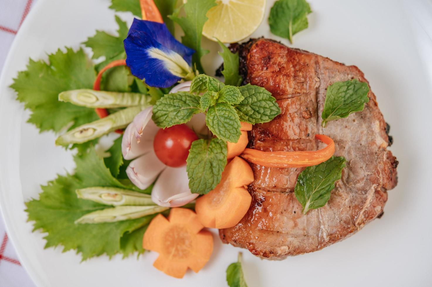 Pork steak with tomato, carrot, red onion, peppermint, butterfly pea flower and lime photo