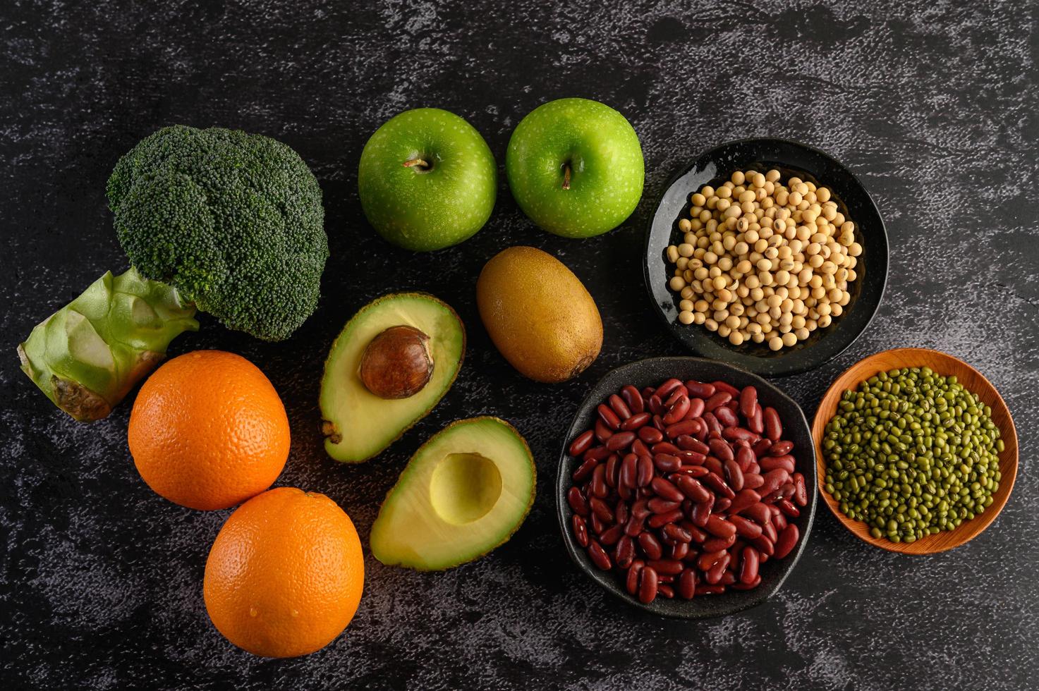 Broccoli, apple, orange, kiwi, avocado and beans on a black cement floor background photo